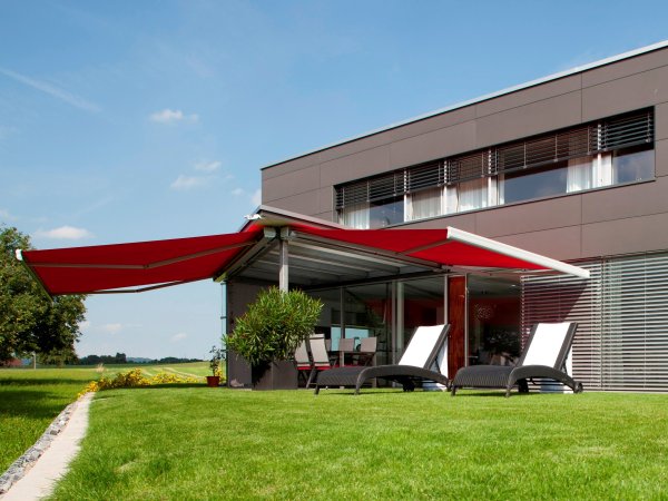 Die hochwertige Hella C2 Kassettenmarkise mit rotem Markisentuch, an einem Wohnhaus mit Flachdach.