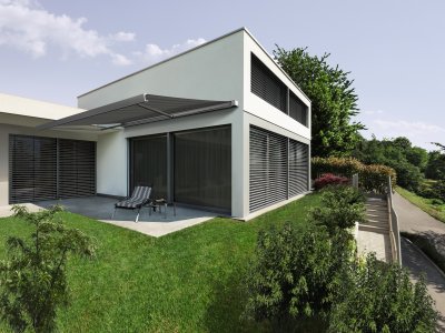 Die Warema Kassettenmarkise K50 an einem Wohnhaus am Hang mit Außenjalousien.