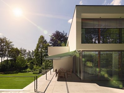 Die offene Gelenkarmmarkise von Frimey an einem modernen Kubus Haus und einer Terrasse.