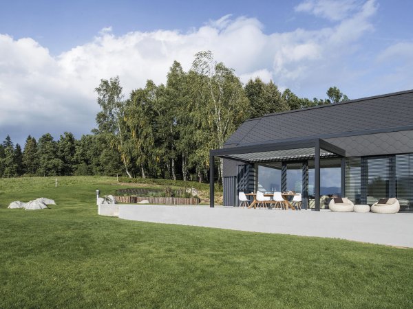 Das bioklimatische Lamellendach Varia von Gibus seitlich am Haus auf einer sonnigen Terrasse mit Esstisch und einem großartigen Ausblick.