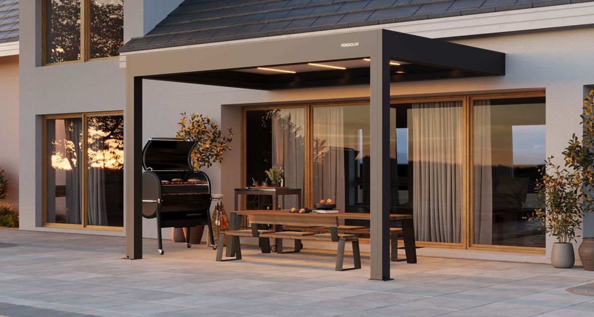 Die Pergola S4 Pro Max von Pergolux in Anthrazit mit weißen Lamellen, direkt an der Hauswand als Wohnzimmer im Freien, bei Frimey GmbH.