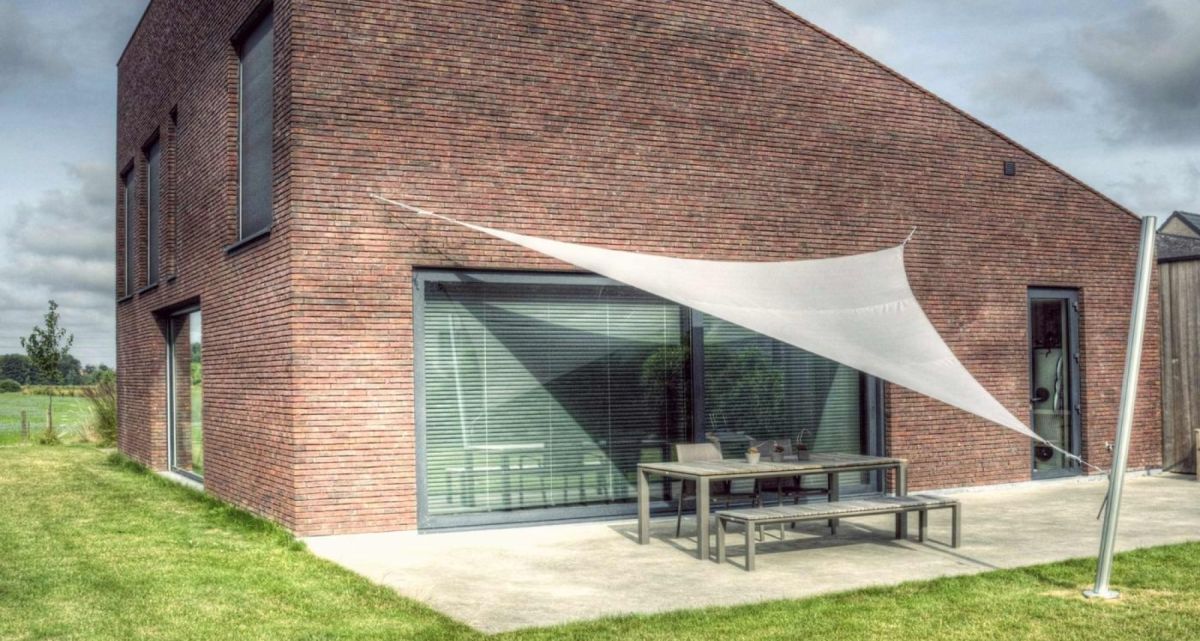 Das in der Höhe verstellbare Sonnensegel Ingenua von Umbrosa an einem puristischen Klinkerhaus, bei Frimey GmbH.